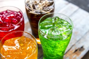 Das Bild zeigt 4 zuckersüße Getränke in den Farben Rot, Gelb, Grün und Dunkel (Cola).